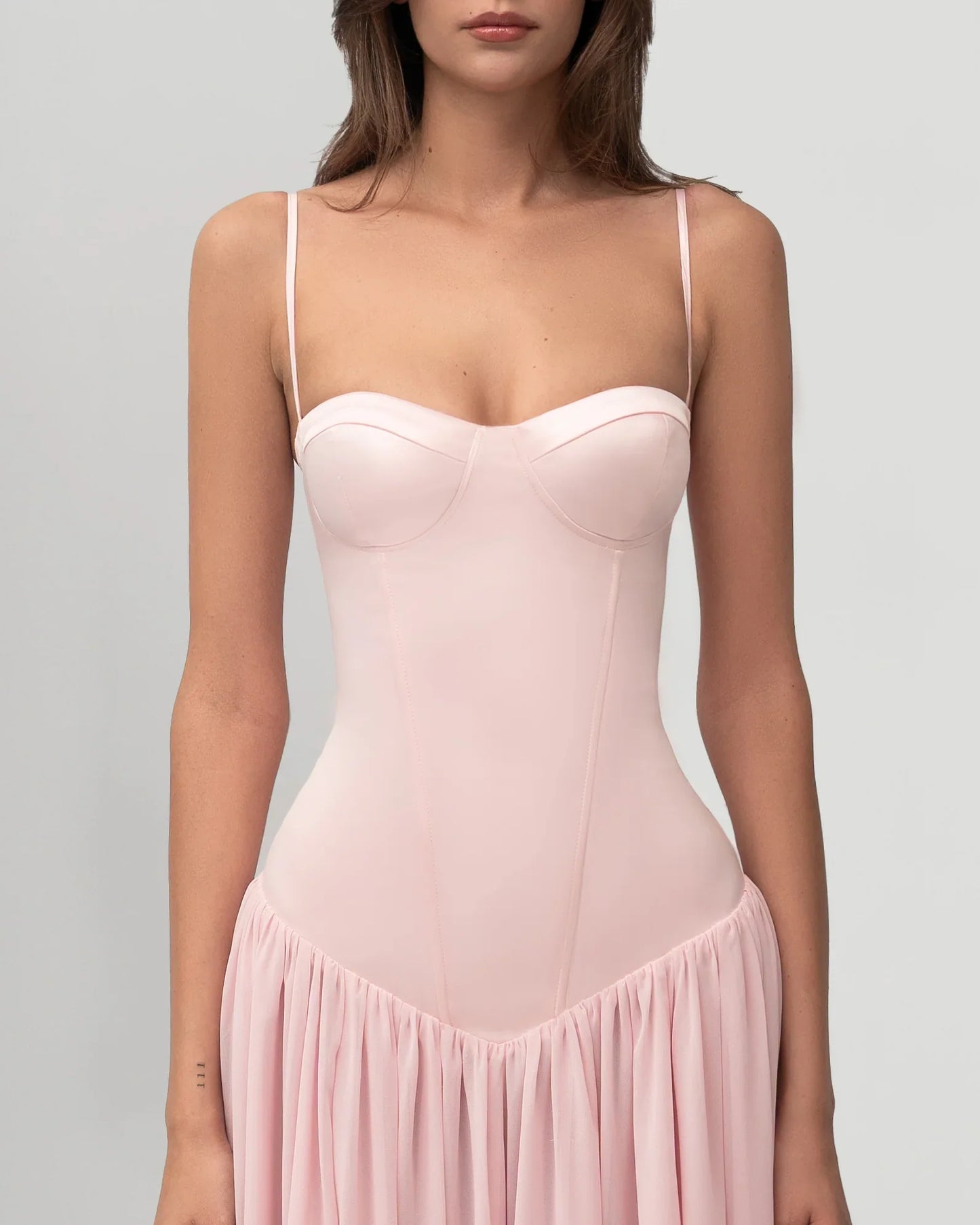 A woman wearing a light pink formal maxi dress featuring a structured corset bodice with spaghetti straps and a flowing, gathered skirt.