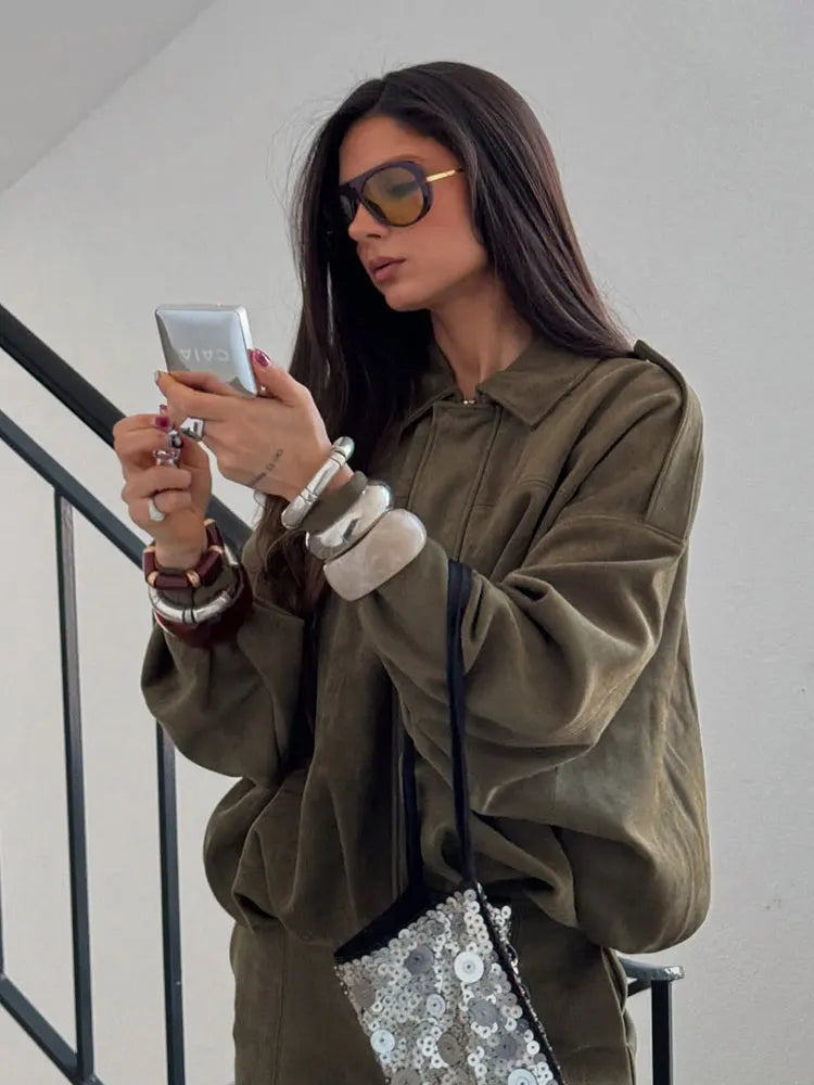 Green - A woman taking a mirror selfie wearing an oversized, olive green faux-suede jacket with dropped shoulders, styled over a white top and dark grey jeans.