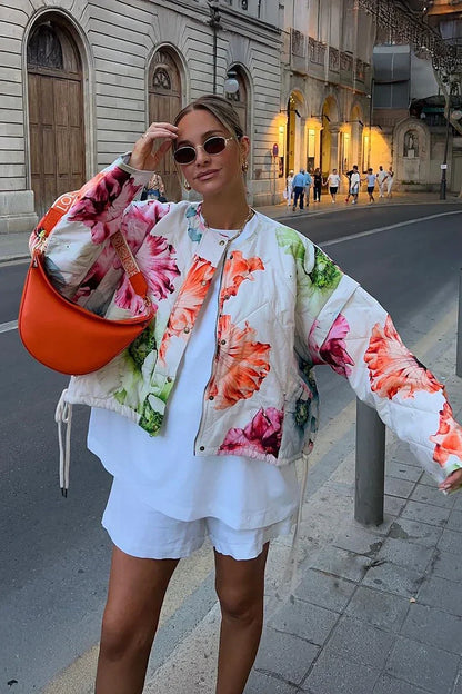 Women's oversized, cropped quilted jacket featuring a bold, large-scale floral print on a light background, styled with a snap-button front and drawstring hem.