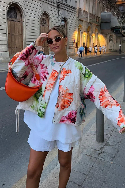 Women's oversized, cropped quilted jacket featuring a bold, large-scale floral print on a light background, styled with a snap-button front and drawstring hem.