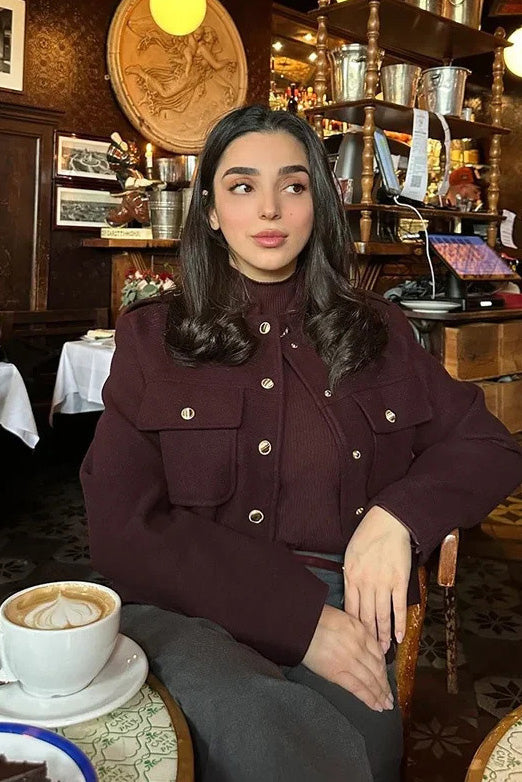 Wine Red - A woman wearing a deep burgundy, military-inspired cropped jacket with gold-tone buttons and chest pockets, paired with grey trousers.