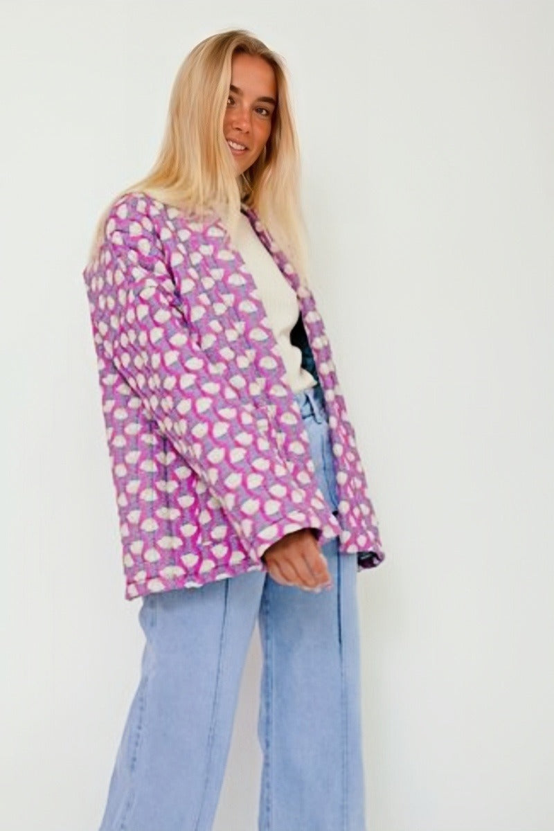 Woman wearing a pink quilted mid-length jacket with a white floral pattern, styled open over a white top and light blue jeans.