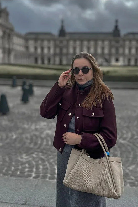 Wine Red - A woman wearing a deep burgundy, military-inspired cropped jacket with gold-tone buttons and chest pockets, paired with grey trousers.