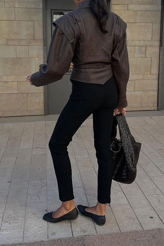 Wine Red - A woman wearing a dark brown, structured wrap faux leather jacket with a tie waist, pronounced shoulders with lace-up details, and a pointed peplum hem.