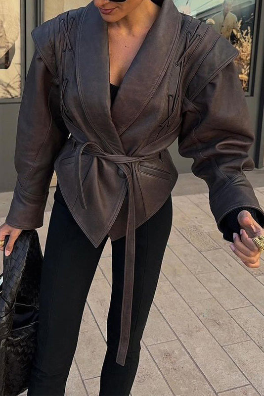 Wine Red - A woman wearing a dark brown, structured wrap faux leather jacket with a tie waist, pronounced shoulders with lace-up details, and a pointed peplum hem.