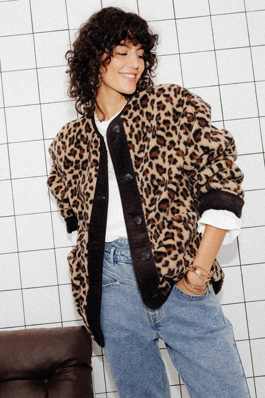 A woman wearing a relaxed-fit, fuzzy knit cardigan featuring a bold leopard print and contrasting dark ribbed placket, styled open over a white top and blue jeans.