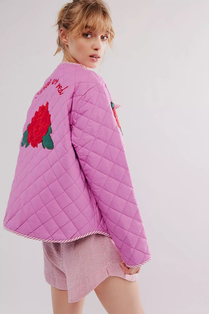 Women's pink diamond-quilted jacket featuring large red rose appliqués, striped tie-front closures, and matching piped edges, worn over a white top and pink striped shorts.