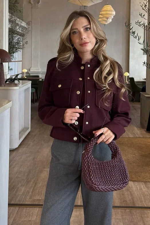 Wine Red - A woman wearing a deep burgundy, military-inspired cropped jacket with gold-tone buttons and chest pockets, paired with grey trousers.