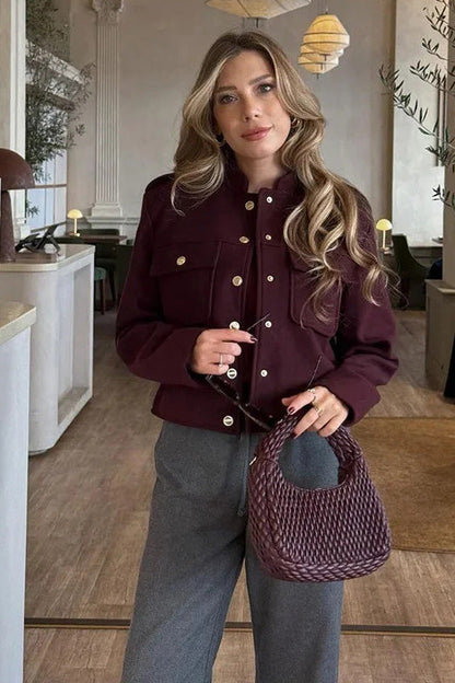 Wine Red - A woman wearing a deep burgundy, military-inspired cropped jacket with gold-tone buttons and chest pockets, paired with grey trousers.