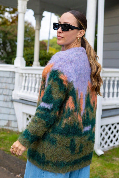 Multi - Woman wearing an oversized, fluffy knit cardigan featuring an abstract landscape pattern in shades of green, purple, and orange over a black turtleneck.