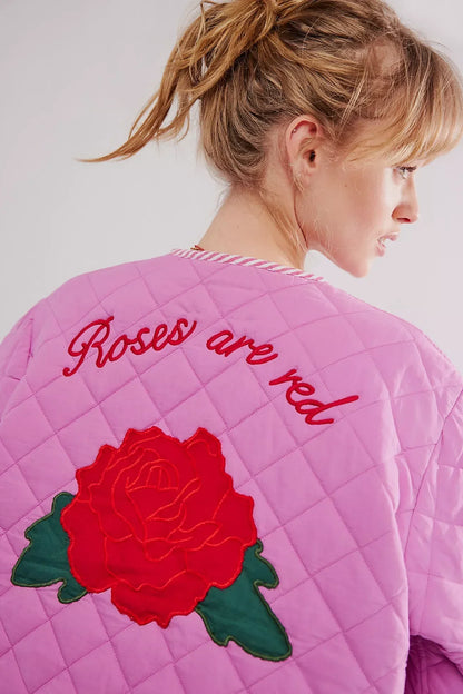 Women's pink diamond-quilted jacket featuring large red rose appliqués, striped tie-front closures, and matching piped edges, worn over a white top and pink striped shorts.