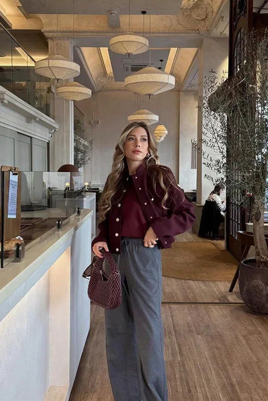Wine Red - A woman wearing a deep burgundy, military-inspired cropped jacket with gold-tone buttons and chest pockets, paired with grey trousers.