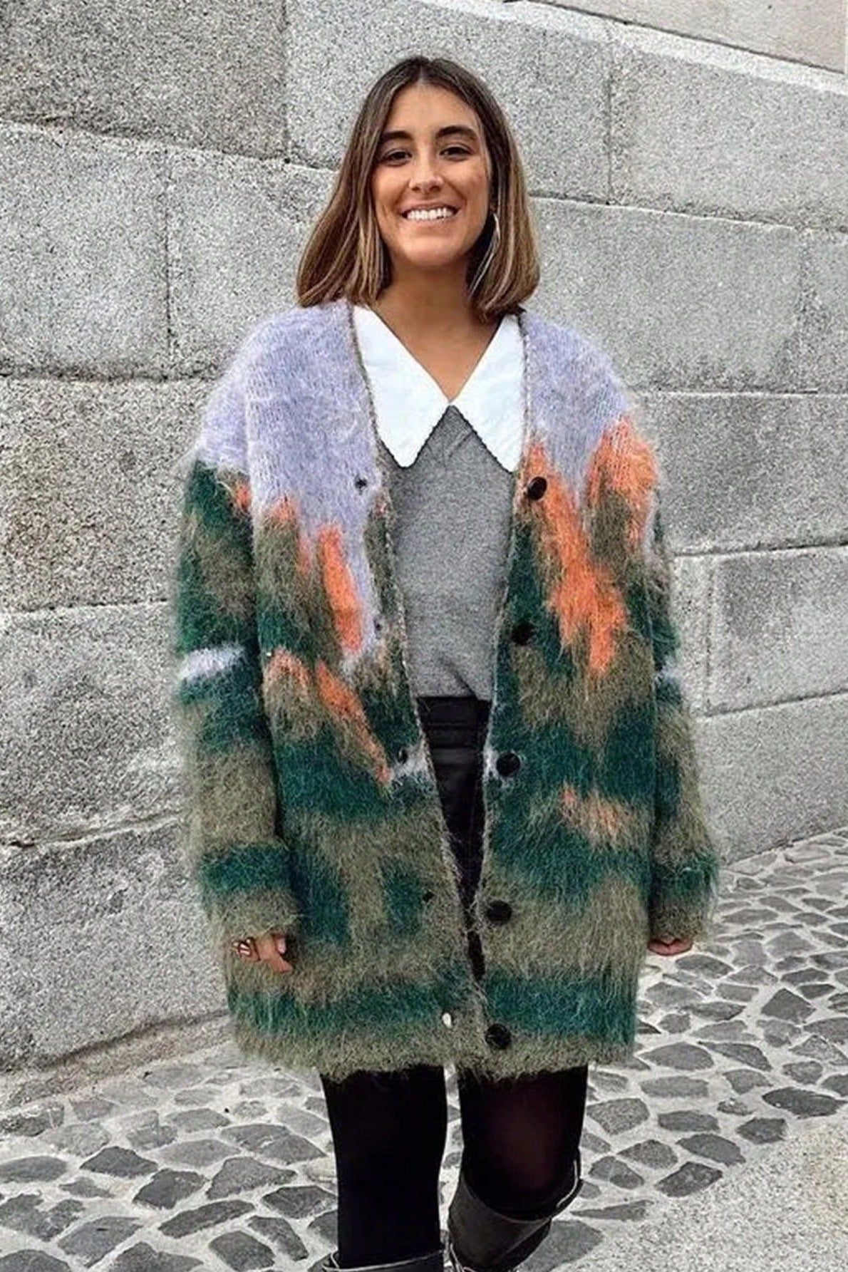 Multi - Woman wearing an oversized, fluffy knit cardigan featuring an abstract landscape pattern in shades of green, purple, and orange over a black turtleneck.
