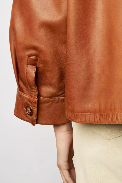 Brown - A woman wearing a relaxed-fit, brown faux leather button-front jacket with a classic collar and single chest pocket, styled over a patterned knit sweater.