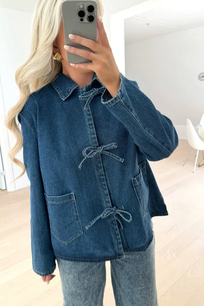 A woman taking a mirror selfie wearing a blue denim jacket featuring three tie-front closures and patch pockets, paired with wide-leg denim trousers.