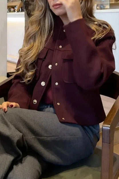Wine Red - A woman wearing a deep burgundy, military-inspired cropped jacket with gold-tone buttons and chest pockets, paired with grey trousers.