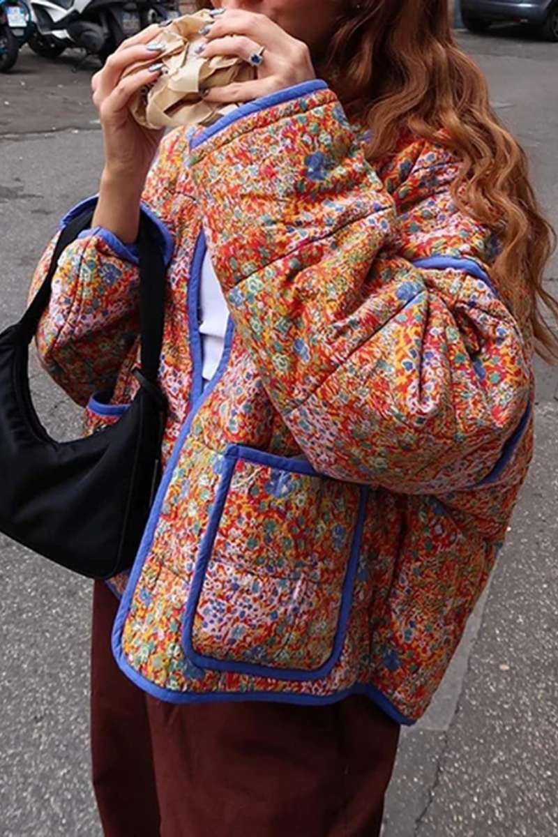 Women's relaxed-fit quilted jacket featuring a vibrant floral print, contrast blue binding on the edges and cuffs, and front patch pockets, worn open.