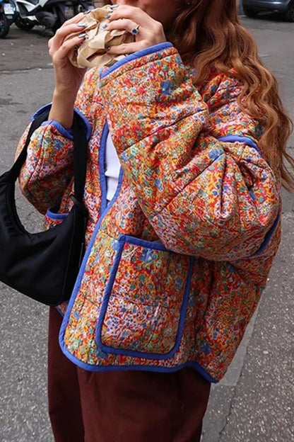 Women's relaxed-fit quilted jacket featuring a vibrant floral print, contrast blue binding on the edges and cuffs, and front patch pockets, worn open.