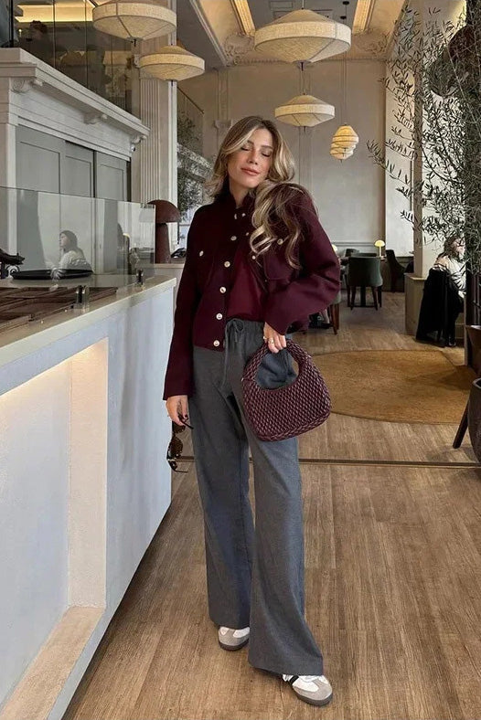 Wine Red - A woman wearing a deep burgundy, military-inspired cropped jacket with gold-tone buttons and chest pockets, paired with grey trousers.