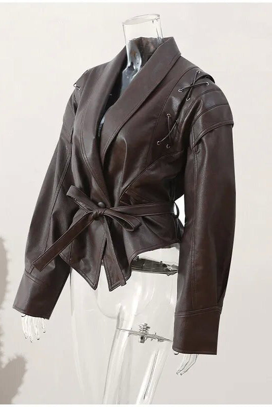 Wine Red - A woman wearing a dark brown, structured wrap faux leather jacket with a tie waist, pronounced shoulders with lace-up details, and a pointed peplum hem.