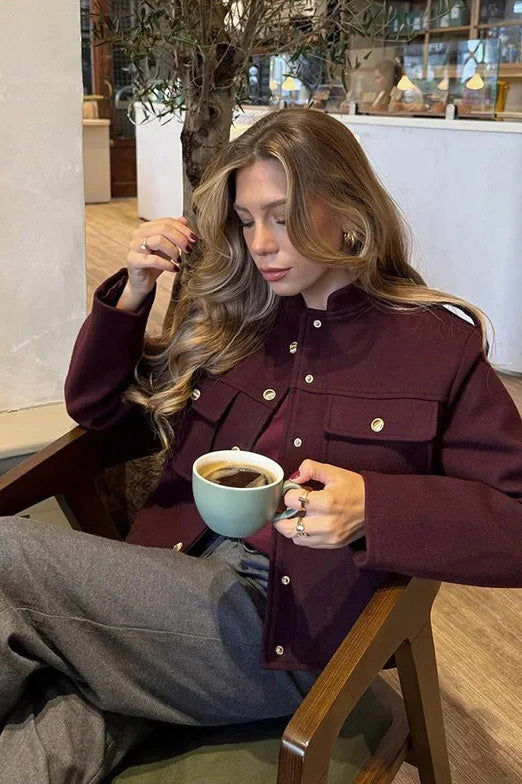 Wine Red - A woman wearing a deep burgundy, military-inspired cropped jacket with gold-tone buttons and chest pockets, paired with grey trousers.