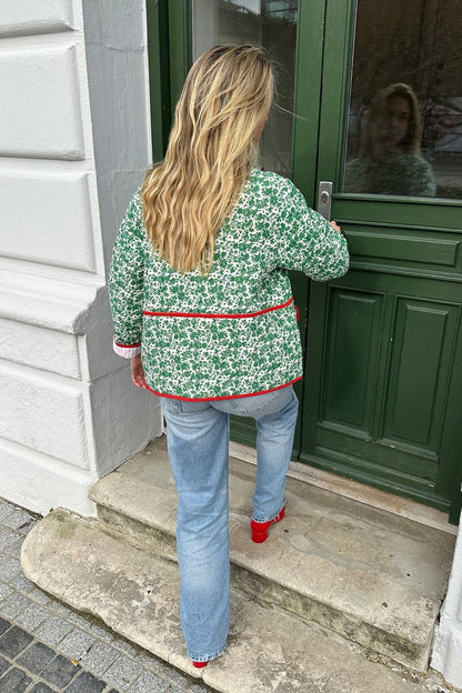 Woman wearing a green and white ditsy floral quilted jacket with red piped trim over a pink striped dress.