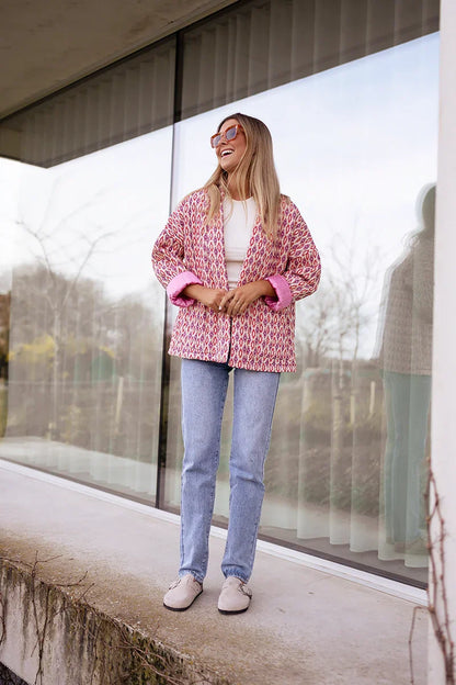 Woman wearing a pink and red geometric print quilted open-front jacket with rolled cuffs, styled with light wash jeans and a white tee.