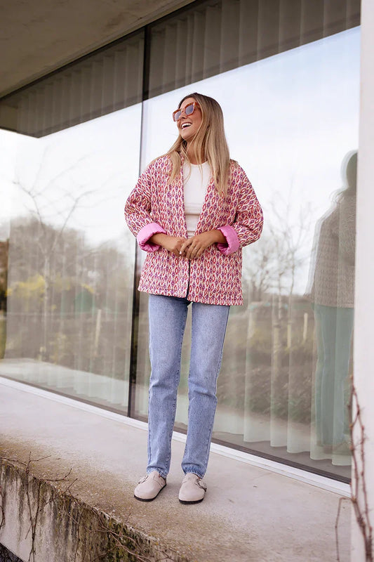 Woman wearing a pink and red geometric print quilted open-front jacket with rolled cuffs, styled with light wash jeans and a white tee.