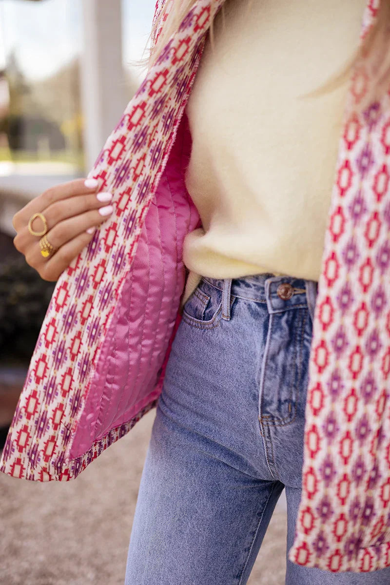 Woman wearing a pink and red geometric print quilted open-front jacket with rolled cuffs, styled with light wash jeans and a white tee.