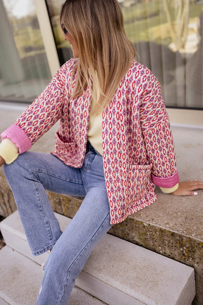 Woman wearing a pink and red geometric print quilted open-front jacket with rolled cuffs, styled with light wash jeans and a white tee.