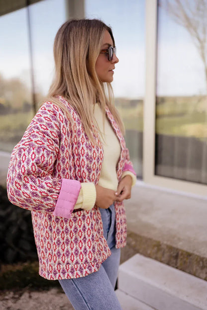 Woman wearing a pink and red geometric print quilted open-front jacket with rolled cuffs, styled with light wash jeans and a white tee.