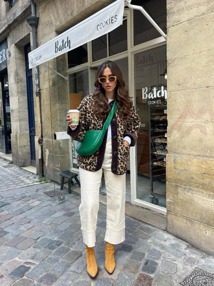 A woman wearing a relaxed-fit, fuzzy knit cardigan featuring a bold leopard print and contrasting dark ribbed placket, styled open over a white top and blue jeans.