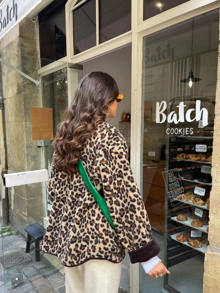 A woman wearing a relaxed-fit, fuzzy knit cardigan featuring a bold leopard print and contrasting dark ribbed placket, styled open over a white top and blue jeans.