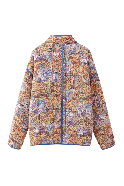 Women's relaxed-fit quilted jacket featuring a vibrant floral print, contrast blue binding on the edges and cuffs, and front patch pockets, worn open.