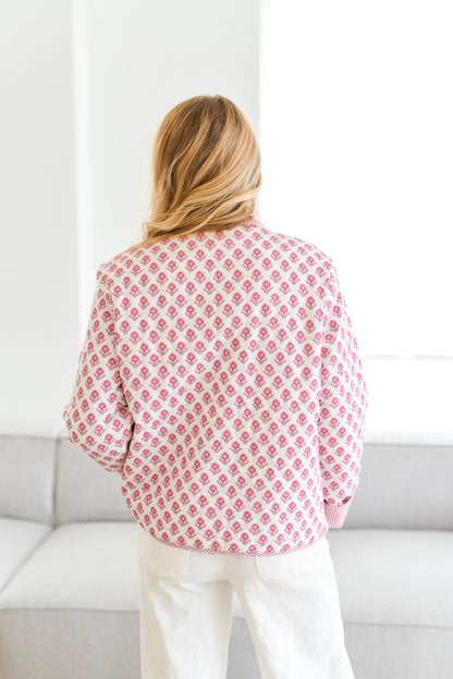 Pink - A woman wearing a white quilted jacket with a pink floral pattern and pink striped collar and cuffs, paired with white jeans.