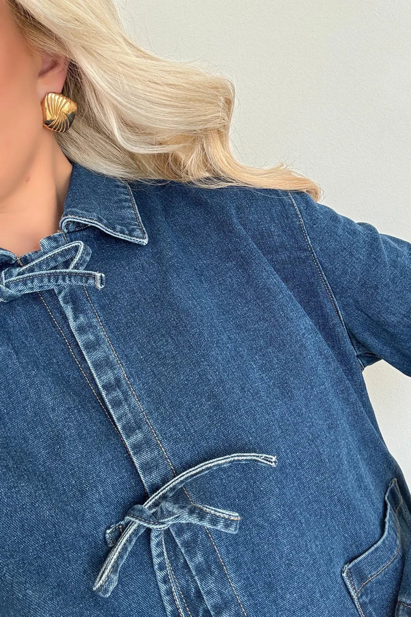 Blue - A woman taking a mirror selfie wearing a blue denim jacket featuring three tie-front closures and patch pockets, paired with wide-leg denim trousers.