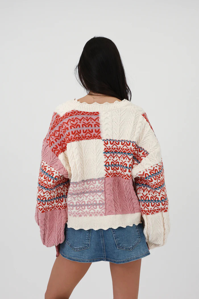 Multi-color - Women's chunky V-neck cardigan featuring a patchwork design of pink, red, and cream Fair Isle patterns and cable knit textures, finished with scalloped edges and metallic buttons.