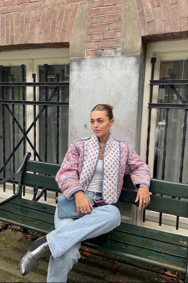 Women's open-front quilted jacket featuring a pink and white floral block print, contrasting blue edge binding, and diamond stitching, worn over a white tee and light wash jeans.