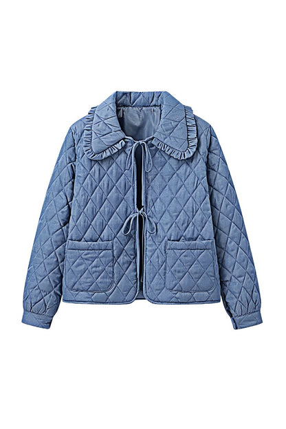 Women's blue diamond-quilted denim jacket featuring a ruffled collar, tie-front closure, and voluminous balloon sleeves, styled with distressed shorts and cowboy boots.