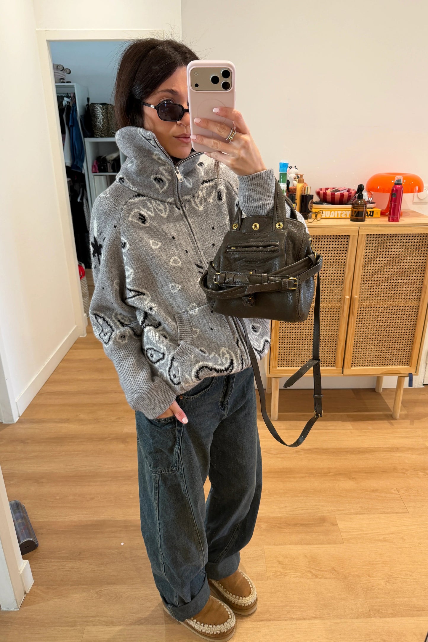 Grey - Woman taking a mirror selfie wearing a grey zip-up knit sweater with a black and white bandana pattern, featuring a high funnel neck and front pockets.