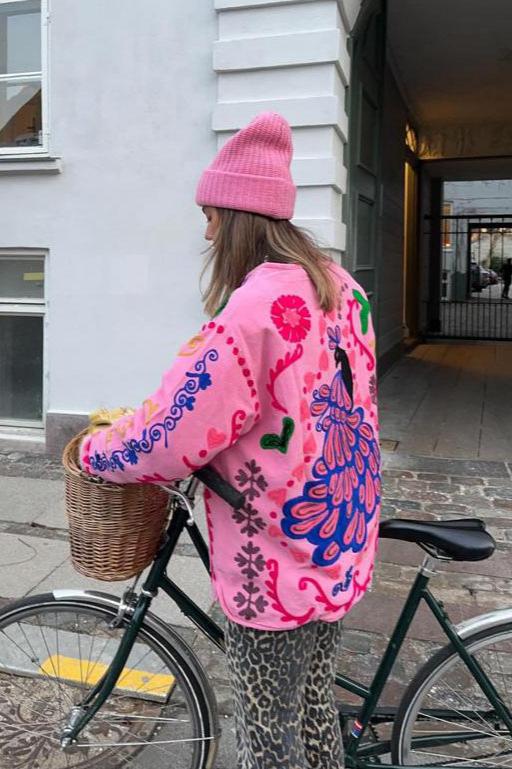 Women's pink long-sleeve relaxed-fit jacket featuring vibrant multi-coloured floral and geometric embroidery, a V-neckline, large contrasting buttons, and front patch pockets.