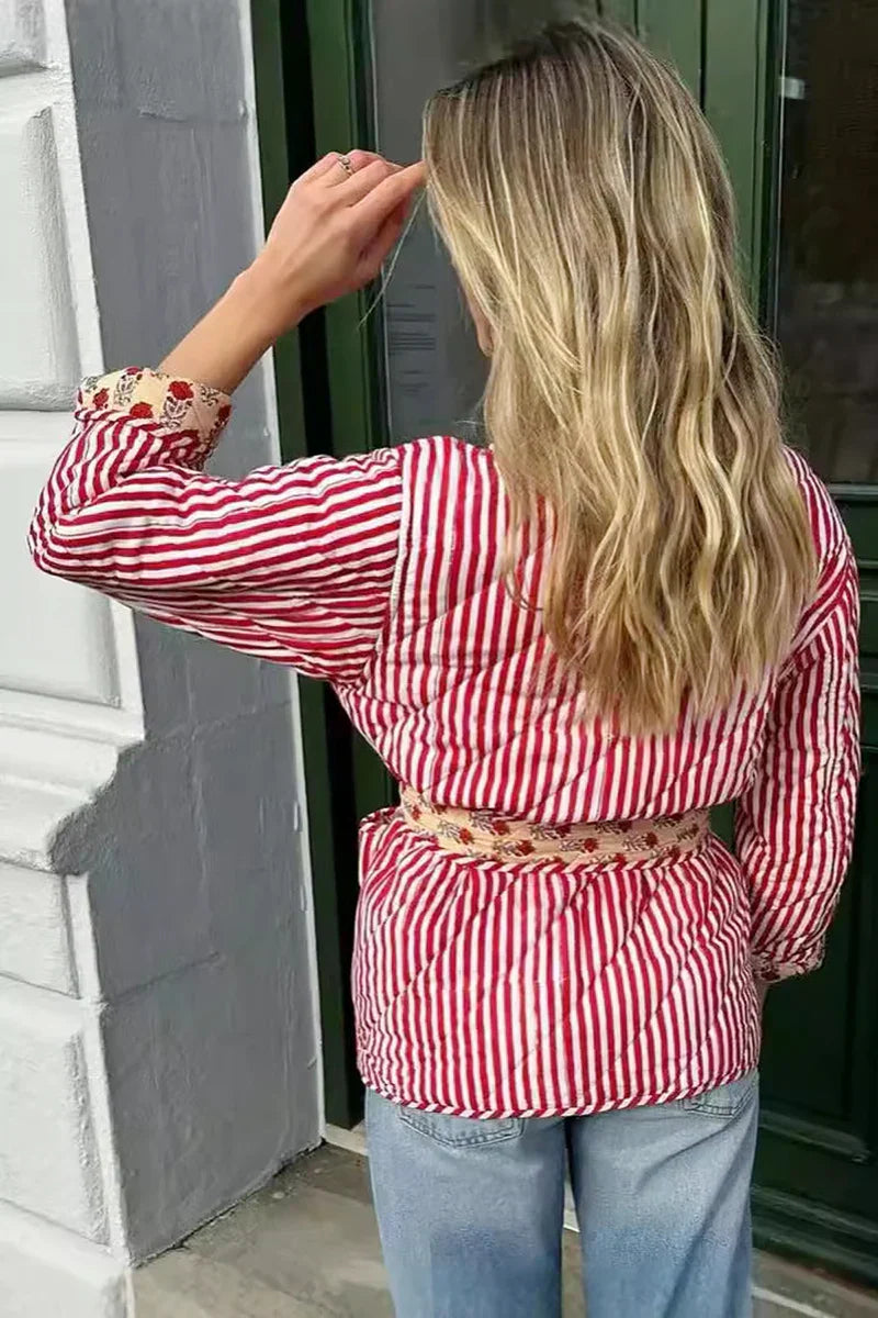 Woman taking a mirror selfie wearing a quilted, cream-coloured wrap jacket with a red floral block print and striped tie belt, paired with blue jeans.