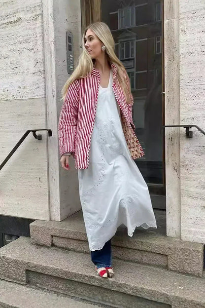Woman taking a mirror selfie wearing a quilted, cream-coloured wrap jacket with a red floral block print and striped tie belt, paired with blue jeans.