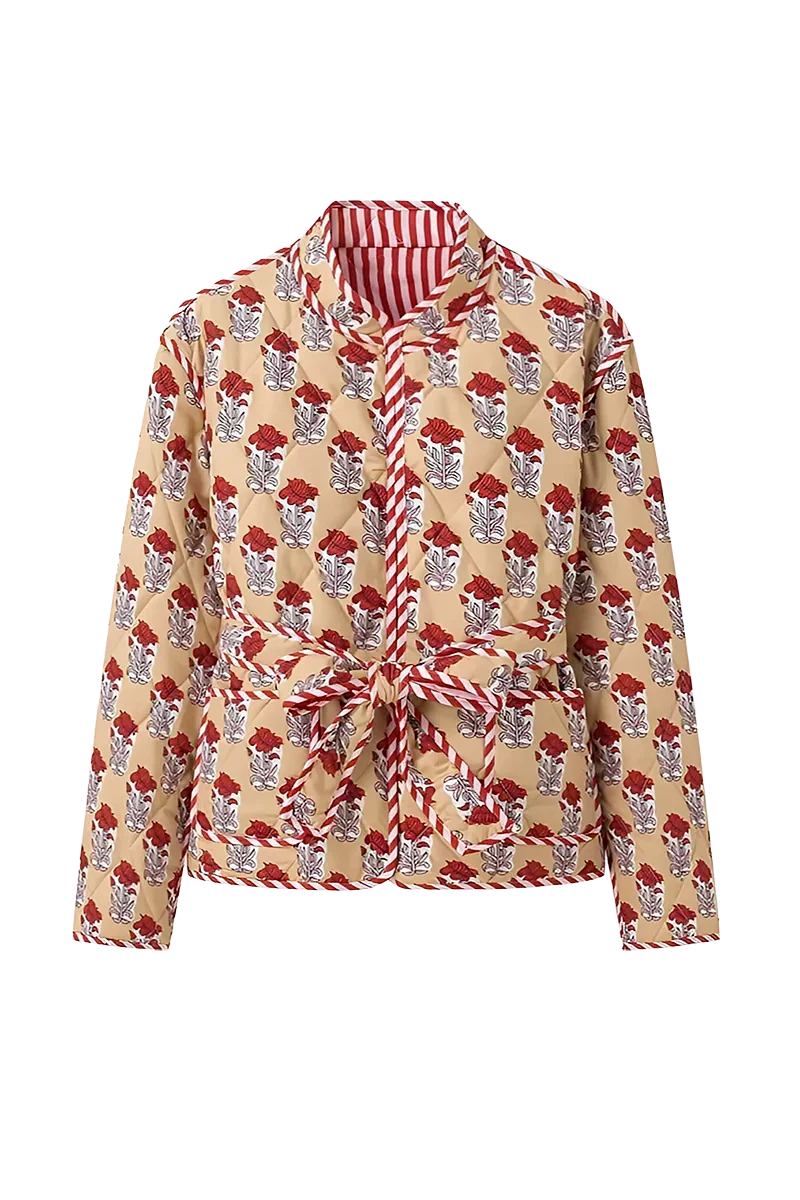 Reversible - Woman taking a mirror selfie wearing a quilted, cream-coloured wrap jacket with a red floral block print and striped tie belt, paired with blue jeans.
