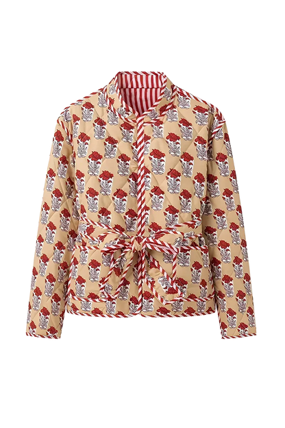 Reversible - Woman taking a mirror selfie wearing a quilted, cream-coloured wrap jacket with a red floral block print and striped tie belt, paired with blue jeans.