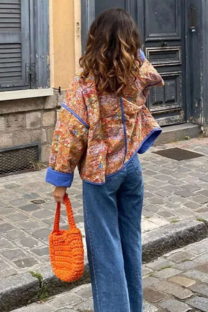 Women's relaxed-fit quilted jacket featuring a vibrant floral print, contrast blue binding on the edges and cuffs, and front patch pockets, worn open.