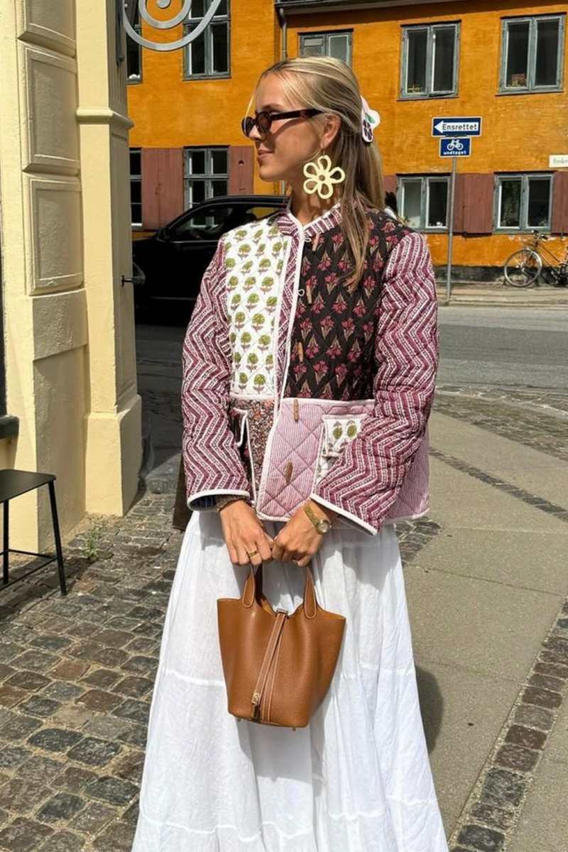 Woman wearing a quilted patchwork jacket featuring mixed floral and chevron prints, paired with a white maxi skirt.