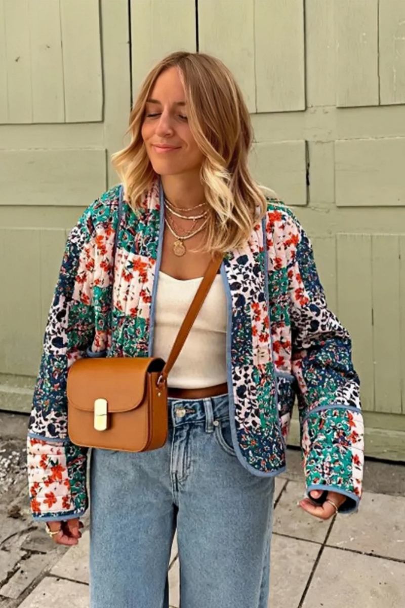 Woman wearing a quilted patchwork jacket with floral prints over a white tube top and blue jeans, standing outdoors.