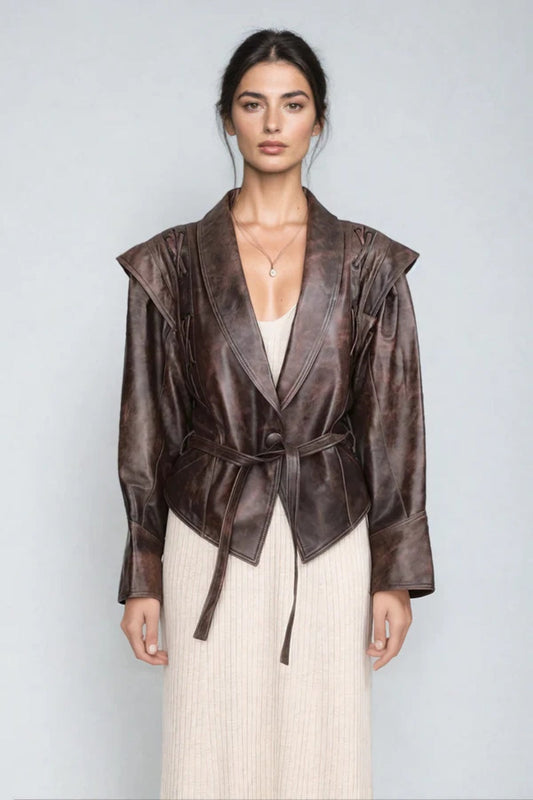 Brown - A woman wearing a brown distressed faux leather jacket with oversized shoulders, lacing details, and a tie belt at the waist, styled over a light ribbed dress.