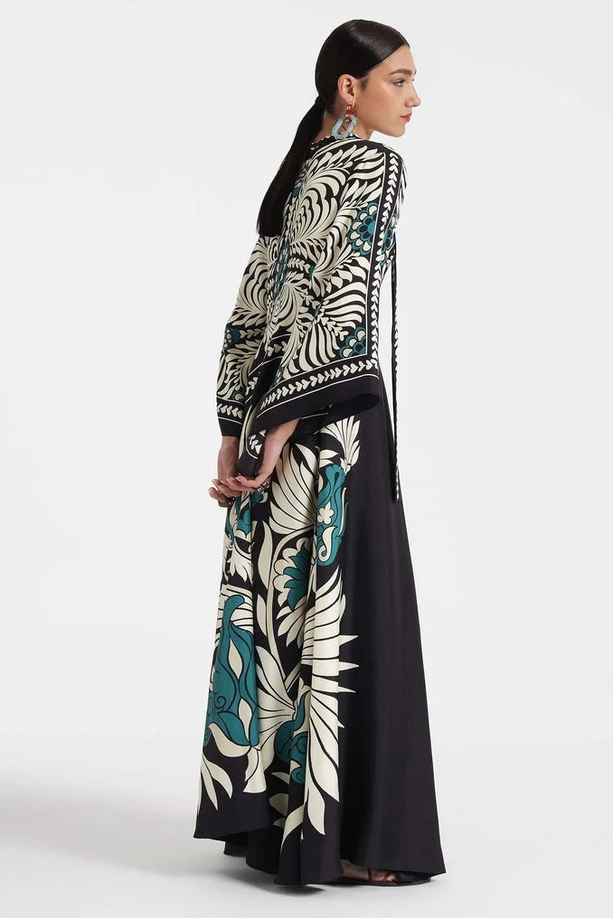 Multi - A woman wearing a high-neck maxi dress with a bold engineered botanical print in black, cream, and teal, featuring wide cape sleeves and a fluid, floor-length drape.
